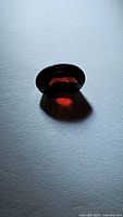 Close-up photo of a single deep cherry red oval cut garnet gemstone with light reflection showing facets and clarity.