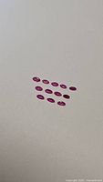 Twelve marquis cut natural ruby stones arranged in rows on a neutral background, showcasing their shape and color.