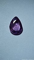 Close-up image of pear-shaped natural pink sapphire gemstone, showing facets and color under light.