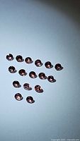 Top-down photo of 17 small round faceted padparadscha sapphires spread randomly on a white surface under bright light