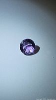 Close-up photo of round faceted purple amethyst gemstone showing color and internal clarity.