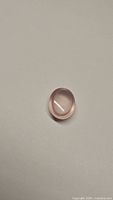 Oval cabochon natural rose quartz gemstone against neutral background, showing size and quality.