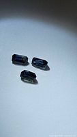 Photo of three natural blue sapphires with octagonal cut placed on white background under light showing shape and color.