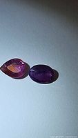 Photo showing oval and pear cut purple-pink sapphires on a light background. Both stones display visible inclusions.