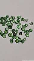 Multiple round cut natural Tsavorite garnet gemstones scattered on a light surface, showing their green color and clarity.