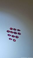 Twelve oval cut rubies arranged on a flat surface, showing rich red color and faceted polish.