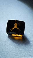 Image showing dark cognac orange yellow cushion cut tourmaline gemstone on light surface with reflections.