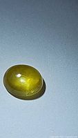 Oval cabochon natural yellow sapphire gemstone on gray background showing its color and surface character.