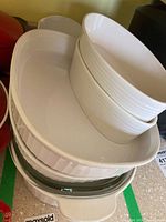 Stack of various ceramic baking and casserole dishes in white and green that are part of the lot