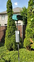 View of the entire bird feeder setup outdoors, showing the green metal feeder mounted on a black pole with the squirrel baffle attached below.