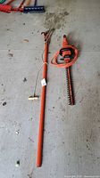 Electric hedge trimmer and manual pole pruner laid out on garage floor, showing general condition and size.