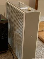 Side and front view of a beige Monarch Aire box fan with handle on top.