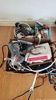 Box containing a variety of cables, power cords, power strips, and surge protectors showing minor visible wear.