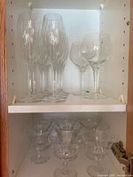 Top shelf with 6 champagne flutes and 2 wine glasses, all clear glass and crystal with etched design.