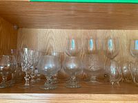 Shelf with an assortment of clear glass stemware including brandy snifters and smaller wine glasses arranged in a row, showing shape and clarity of glassware.
