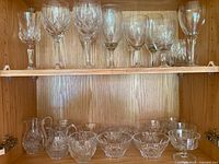 Wide view of glassware collection showing 8 stemmed glasses on the top shelf and 6 smaller glass items including dessert bowls and small pitchers on the bottom shelf.