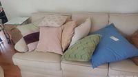 Cushions arranged on beige sofa showing variety of colors including beige, green, blue, and patterned cushions.