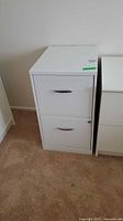 Front view of white 2-drawer file cabinet on carpeted floor, showing drawer handles and lock on lower drawer.