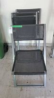 Photo of 3 black metal folding chairs stacked or lined up, showing mesh seats and backs.
