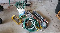 Overview of lot showing hoses coiled with Gardena hose connectors, two oscillating sprinklers, a bucket with green metal garden stakes, and hose nozzle