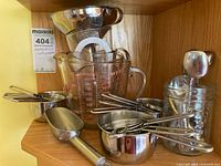 Wide view showing glass measuring cup, metal scoop, metal measuring spoons, funnels stacked inside each other
