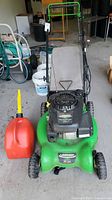 Front view of green Lawn-Boy lawn mower with fabric grass catcher, handlebar with control levers, and included orange gas can.