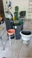 Overview of planters, plant supports, mesh fencing rolls, decorative urn planter, and metal shelving rack in a garage setting