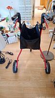 Front view showing black storage bag, ergonomic handles with red brakes, and two rear wheels on red frame.