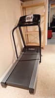 Full side and top view of black PaceMaster Gold Elite VR treadmill in basement with owner's manual on console.