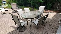Full view of oval glass-top table with six chairs on a brick patio.