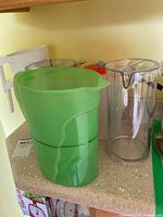 Set of six plastic beverage pitchers including green and clear pitchers visible on counter
