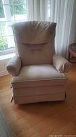 Front view of cream fabric recliner rocker chair showing padded back, armrests and seat.