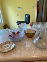 Photo shows a collection of mixed glassware including textured clear bowls, amber amber bowl, frosted carafe, and one Royal Albert china plate with floral and gold pattern.