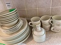 Full view of stacked plates, bowls, cups, saucers, and lidded jar on counter.
