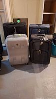 Lot photo showing all 4 suitcases together: two black soft-sided, one navy blue soft-sided, one light grey hard shell