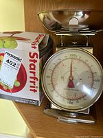 Mechanical Starfrit kitchen scale with stainless steel bowl and original box visible. Dial shows capacity up to 2000g or 4 lb 8 oz.