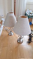 Two table lamps displayed on wooden floor, showing bases and shades