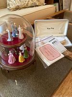 Two-tier wooden display stand holding eight painted porcelain or ceramic Victorian/Edwardian female figurines, with glass dome cover.