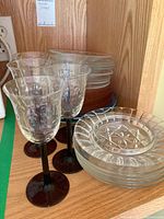 Four vintage clear glass stem glasses with dark brown stems and stacked clear glass plates with pressed starburst designs