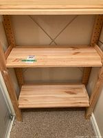 Front view of the wooden shelving unit showing three flat shelves and wooden frame with metal cross brace at the back.