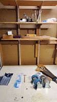 Overview of workshop tools including chisels, casters, saws, mallet, and containers on a workbench with shelves above