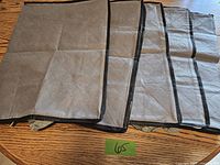 Five beige quilted fabric zipped storage bags laid out flat on a wooden surface, showing black trim and quilted diamond pattern.