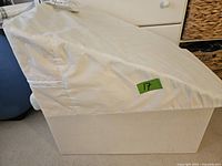 Side view of angled pillow backrest showing the foam base covered by a removable white fabric cover with tag.