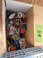 Box filled with assorted embroidered cloth patches and colorful round tokens.