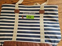 Front view of KeepCool insulated cooler bag with navy and white horizontal stripes, beige carrying handles, and brown accents.