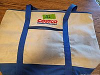 Photo of beige Costco cooler bag with blue handles and logo on front.