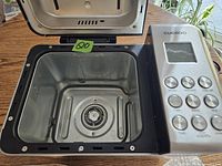 Open bread maker showing empty interior baking chamber with heater and paddle attachment point