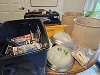 Photo showing black toolbox with tools and supplies, packaged light bulbs, white dome light fixtures, lamp shades, and a smoke detector on a table.