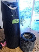 GermGuardian black air purifier standing vertically on a wooden table next to its cylindrical filter, showing purifier vents and power cord