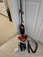 Full view of Gravitti steamer upright unit with cord wrapped and multiple accessories laid on the floor.